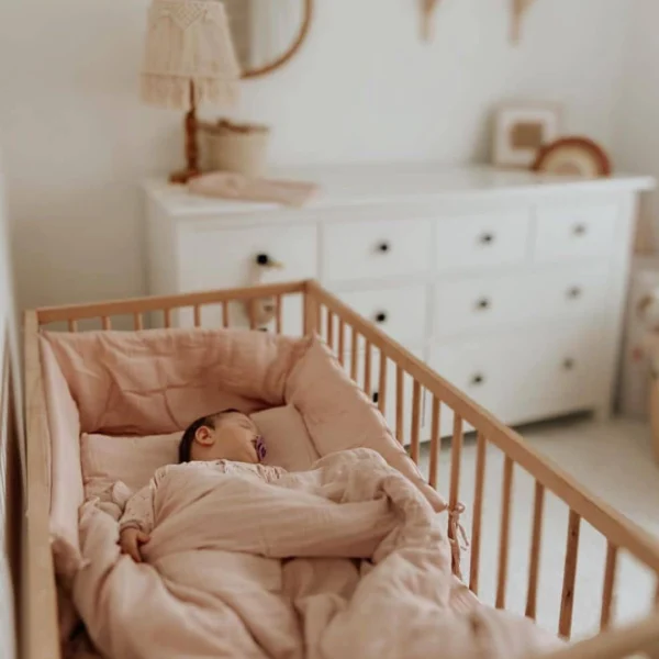 posteljina za bebe od muslina u drvenom krevecu. Beba spava prekrivena prekrivacem u navlaci za prekrivac od muslina