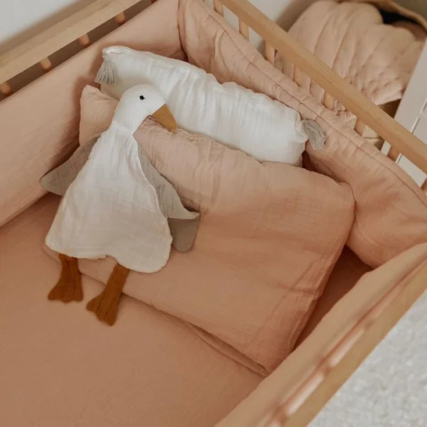 posteljina za bebe od muslina sa ogradicom u krevecu. Na jastuku lezi patkica mazilica bele boje i sivih krila