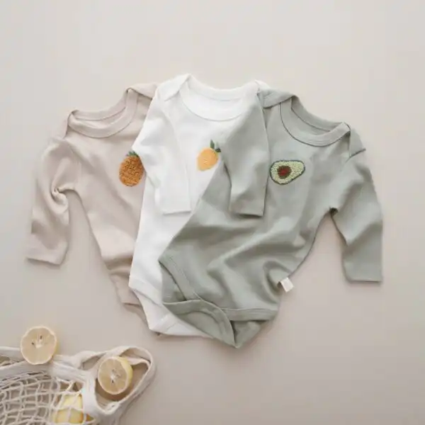 bodici za bebe sa dugim rukavima set zeleni bodi sa vezom avokada beli sa vezom limuna bez sa vezom ananasa razlozeni jedan na drugi na pozadini boje peska