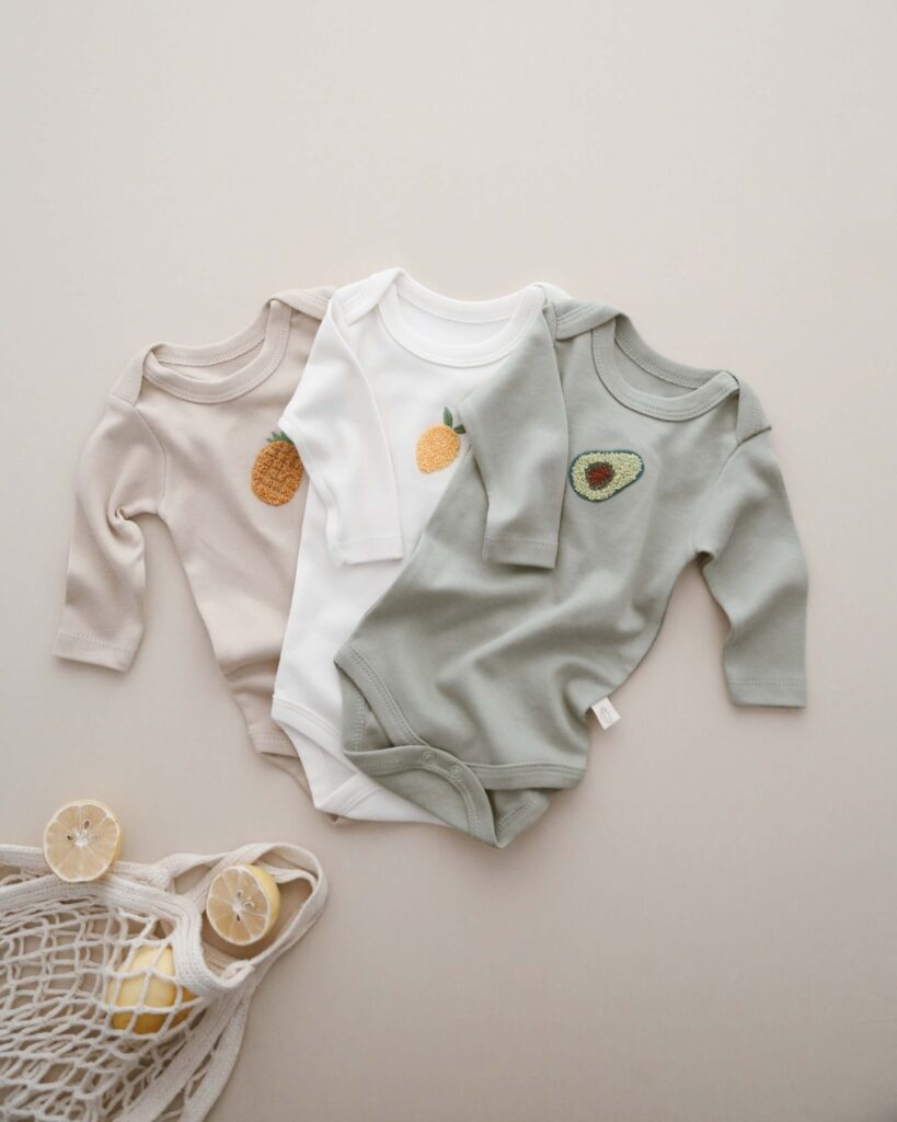 bodici za bebe sa dugim rukavima set zeleni bodi sa vezom avokada beli sa vezom limuna bez sa vezom ananasa razlozeni jedan na drugi na pozadini boje peska