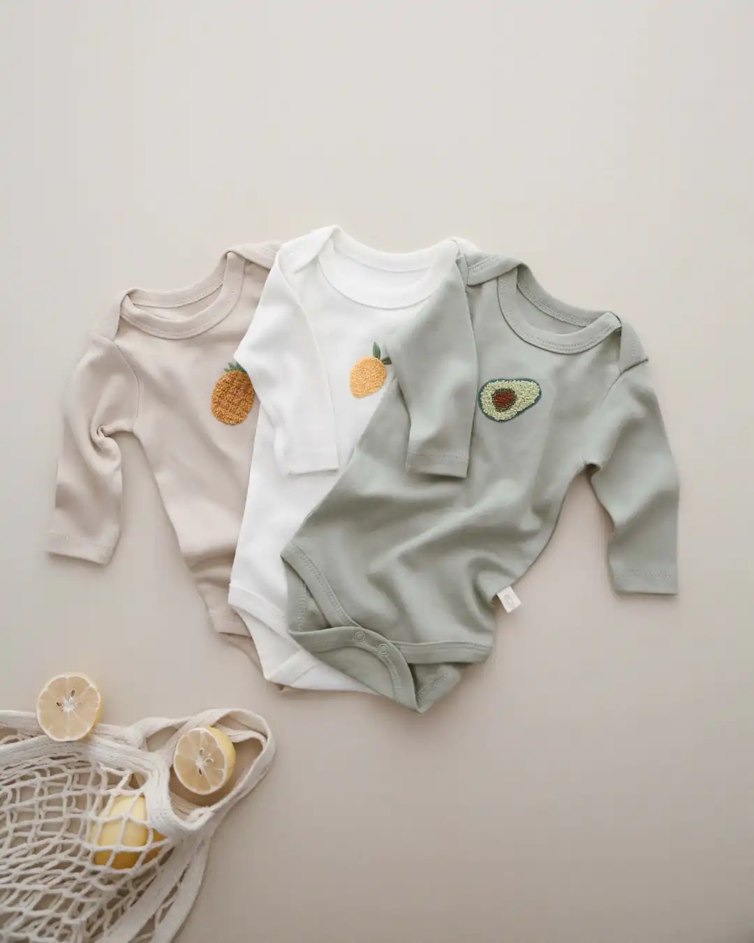 bodici za bebe sa dugim rukavima set zeleni bodi sa vezom avokada beli sa vezom limuna bez sa vezom ananasa razlozeni jedan na drugi na pozadini boje peska