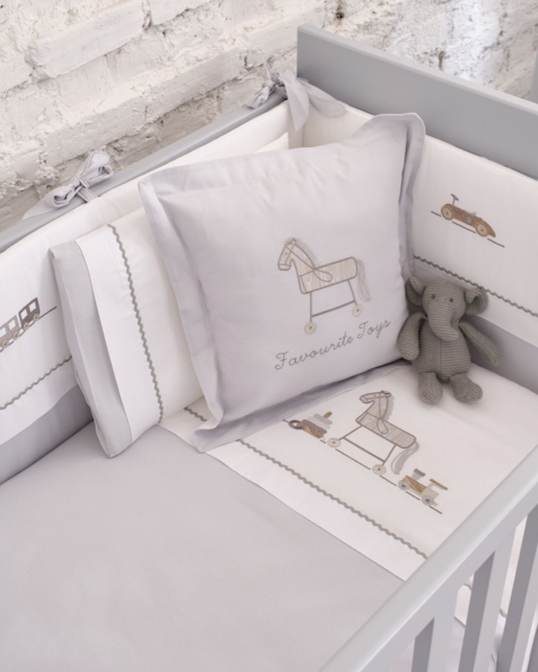 posteljina za bebe set od sedam delova u kombinaciji sive i bele boje sa vezenim motivom igracaka na krevecu