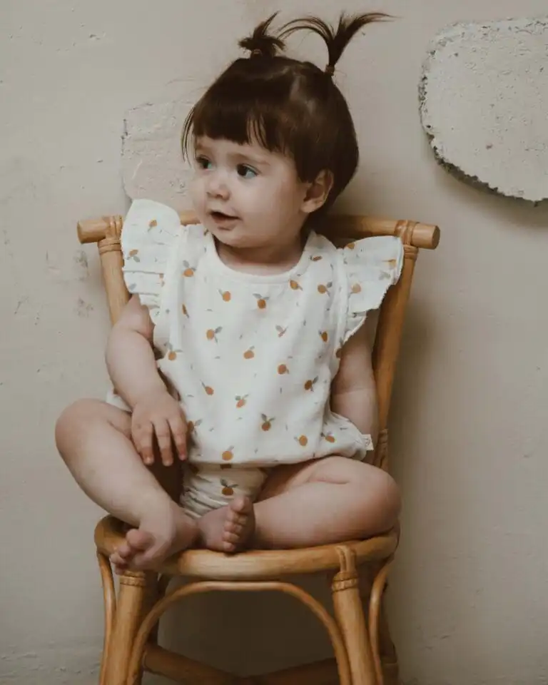 romper od muslina sa karnerom na ramenima krem boje sa motivom pomorandze na devojcici koja sedi na drvenoj stolici