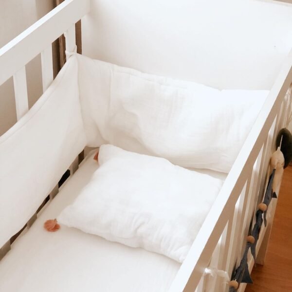 ogradica za bebe od muslina beleboje sa jastukom sa kicankama u kombinacijij sa belom posteljinom na krevecu