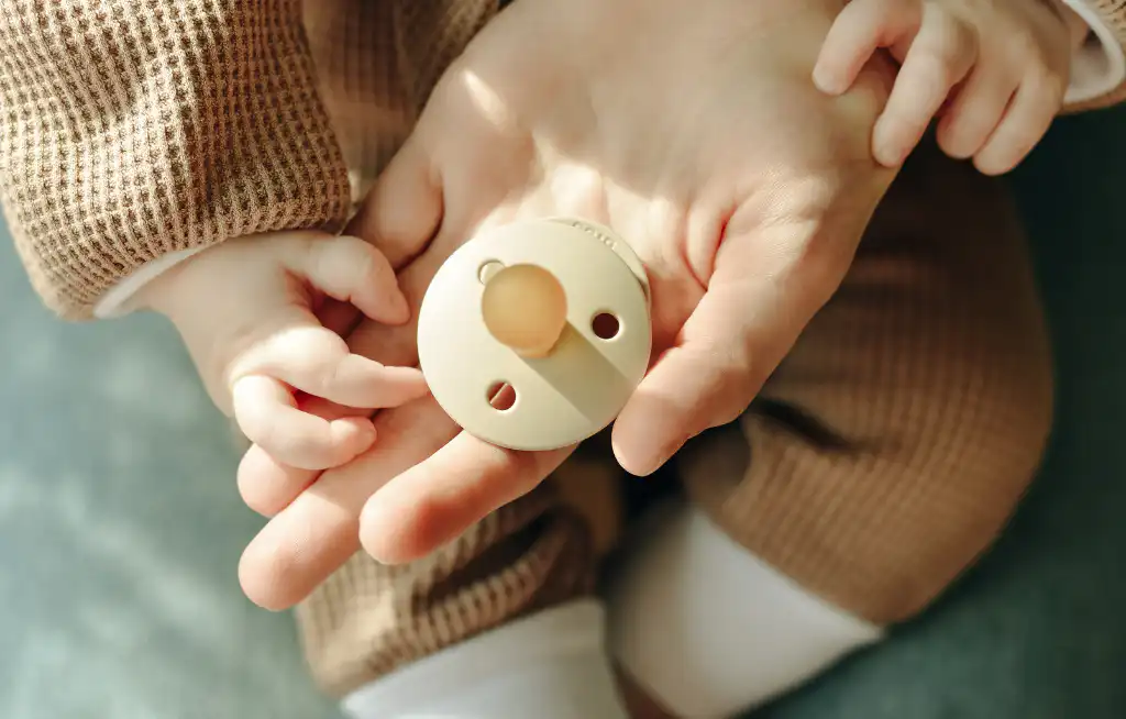 cucle za bebe mama drži bebu u naručju dok u ruci drži cuclu