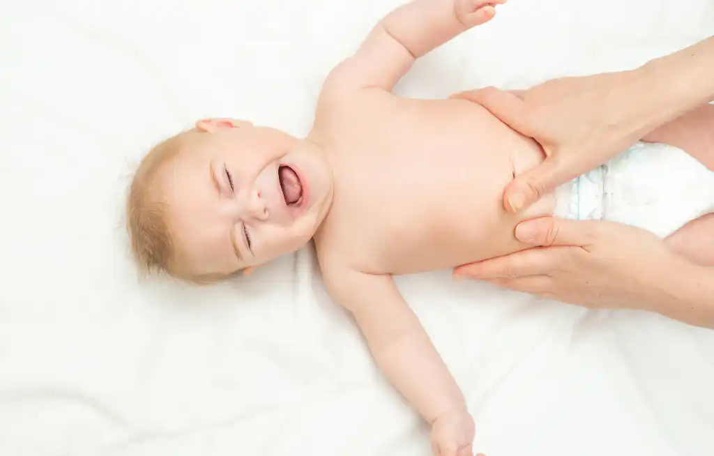 beba leži na leđima na belom čaršafu mama joj masira stomak dok ona plače