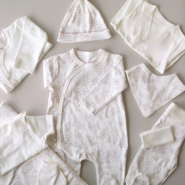 unisex set za iznosenje bebe sa motivom zeke roze boje cebe kombinezon bluzica bodic benkica pantalone kapica portikla rukavice i maramica na pozadini