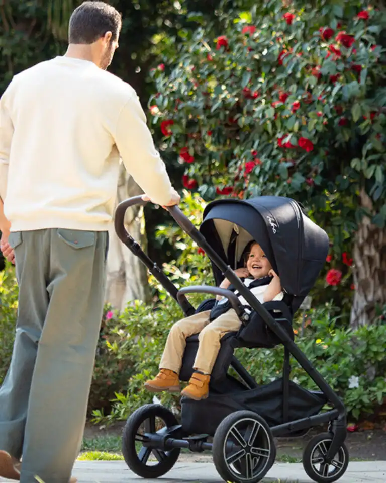 nuna kolica crne boje otac gura bebu u kolicima