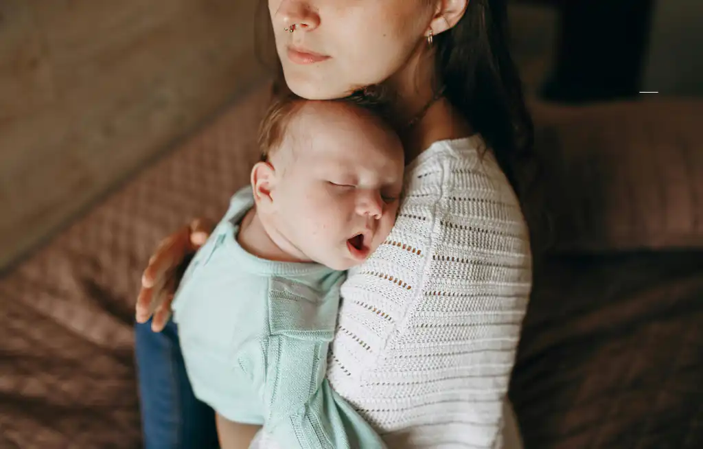 kako uspavati bebu mama drži novorođenče u naručju sa glavom na ramenu