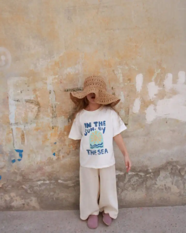 komplet majica u beloj boji sa natpisom in the sun by the sea i print sunca i talasa i krem pantalone